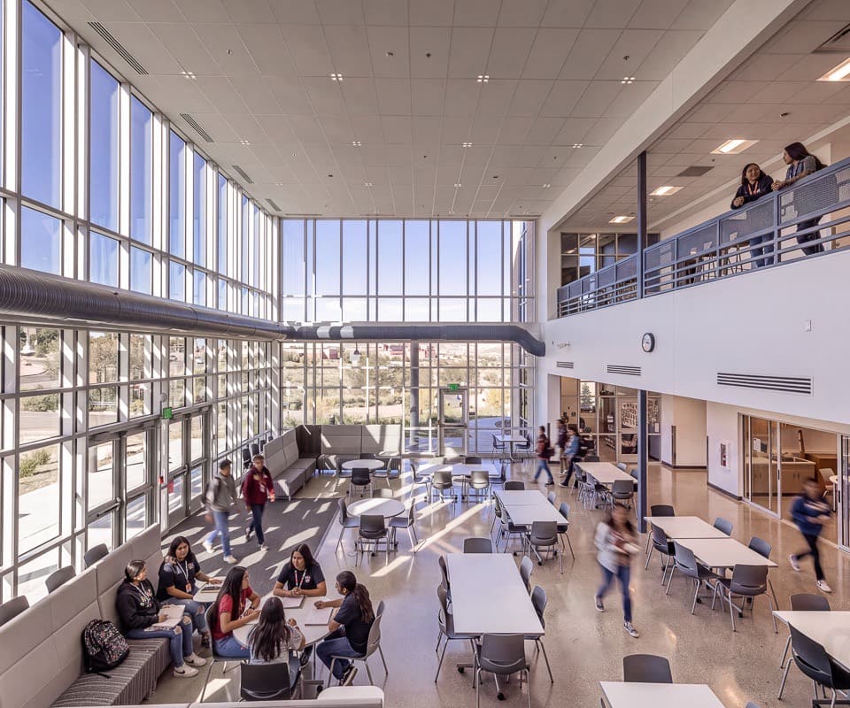 Students at tables in a double-height commons with a wall of glass