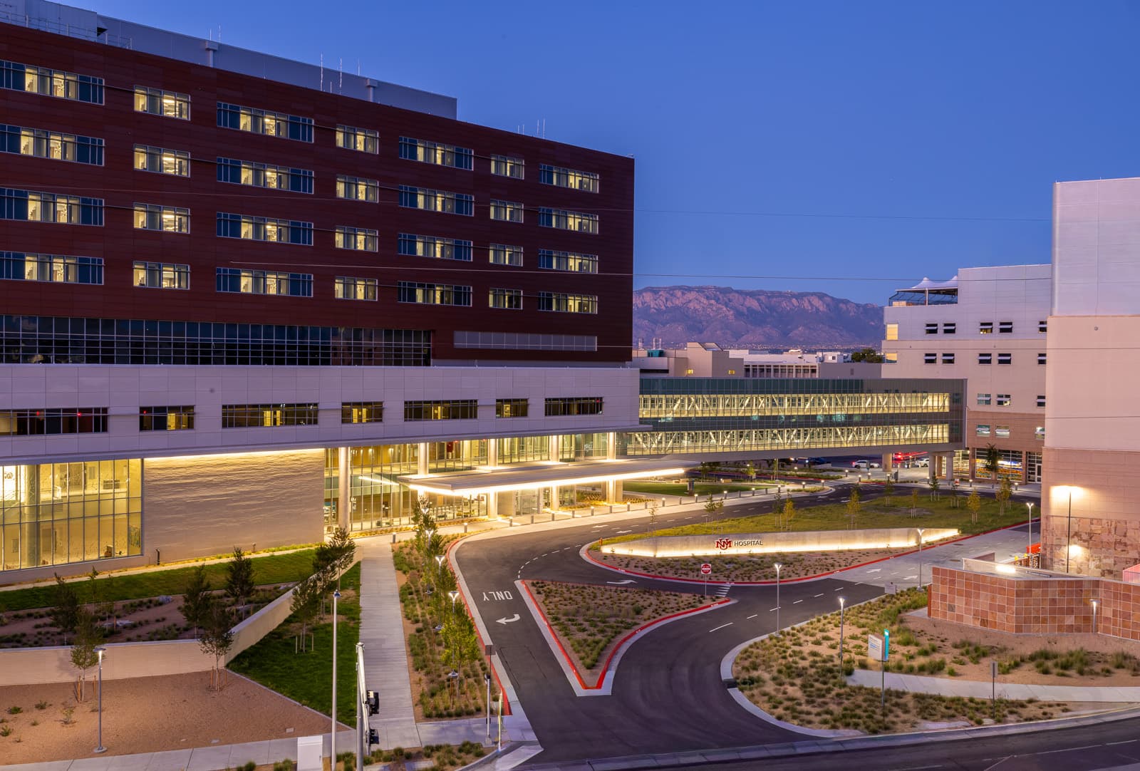 UNM Hospital's Critical Care Tower at dusk, its entry drive lit and the Sandias behind